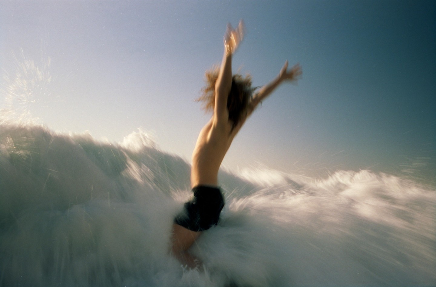 A person with arms raised is partially submerged in a breaking wave.