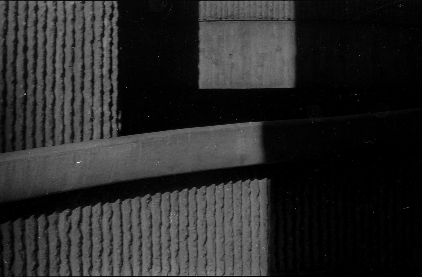 A black and white abstract image shows a textured wall with a diagonal beam and a rectangular shadow.