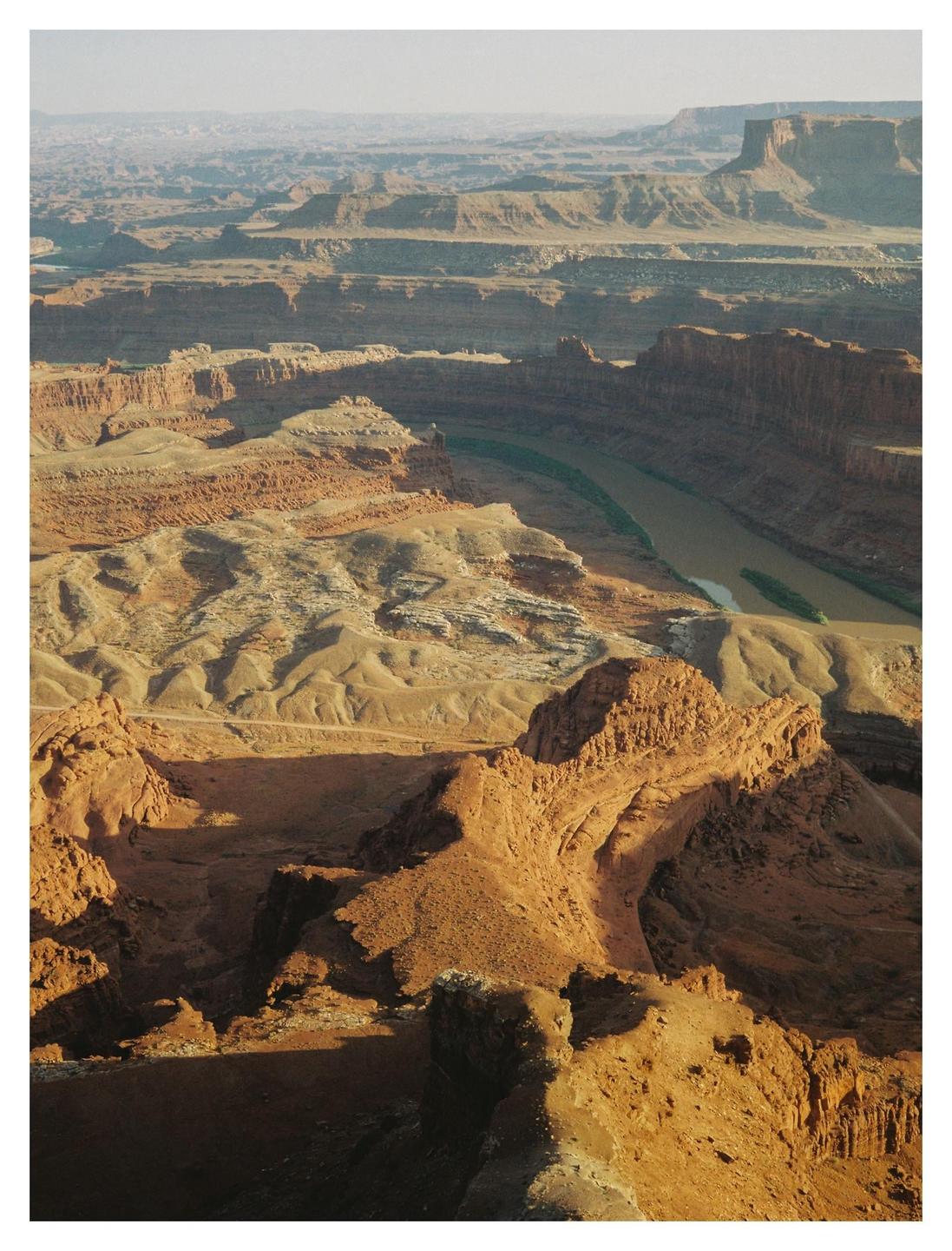 A vast canyon landscape with a river winding through it is visible under a hazy sky.