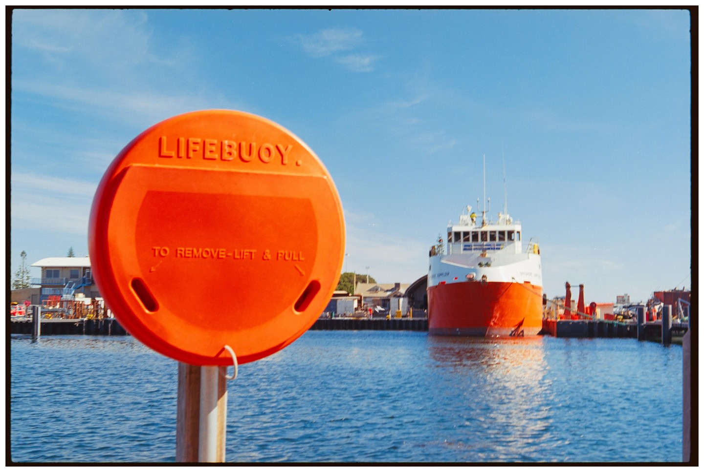 An orange lifebuoy is in the foreground of a harbor with a large ship docked in the background.