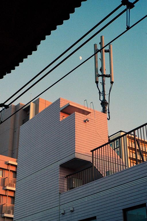 A crescent moon is visible in the sky above buildings and power lines.
