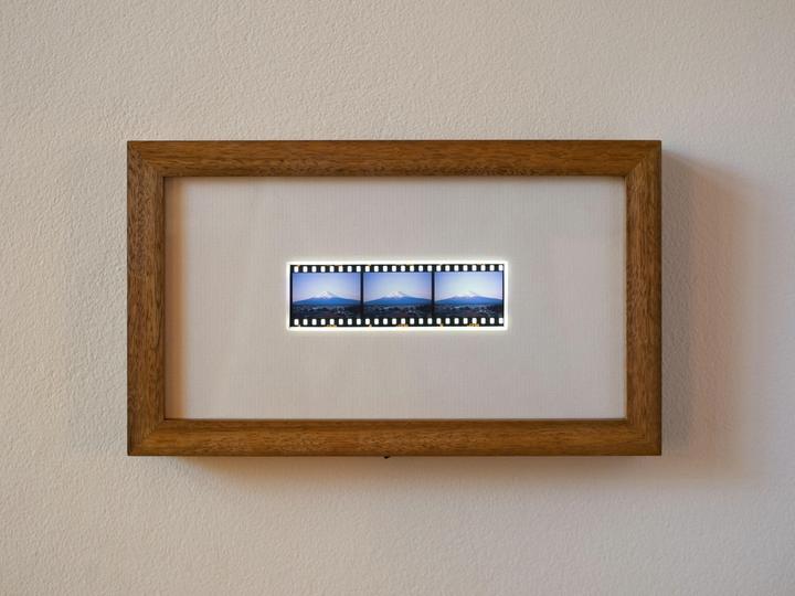 A wooden framed lightbox displays three film negatives of Mount Fuji.