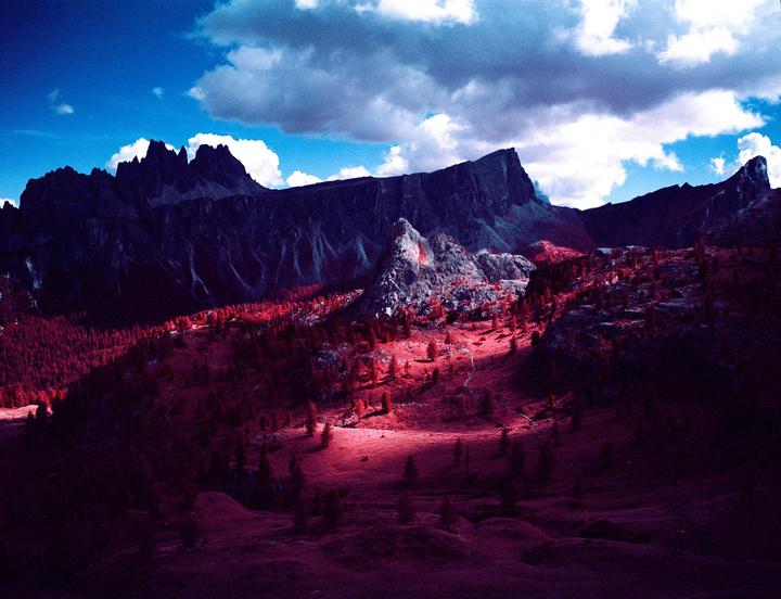 A mountain landscape with red trees and grass is visible under a blue sky with clouds.
