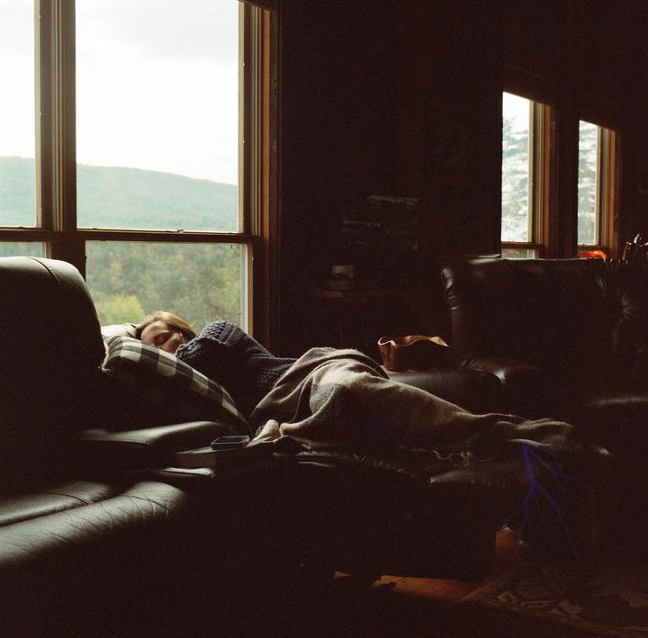 A woman sleeps on a couch next to a window overlooking a mountain.
