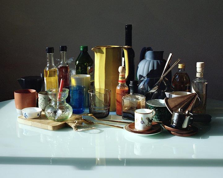 A collection of kitchen items, including bottles, glasses, and cups, is arranged on a reflective surface.