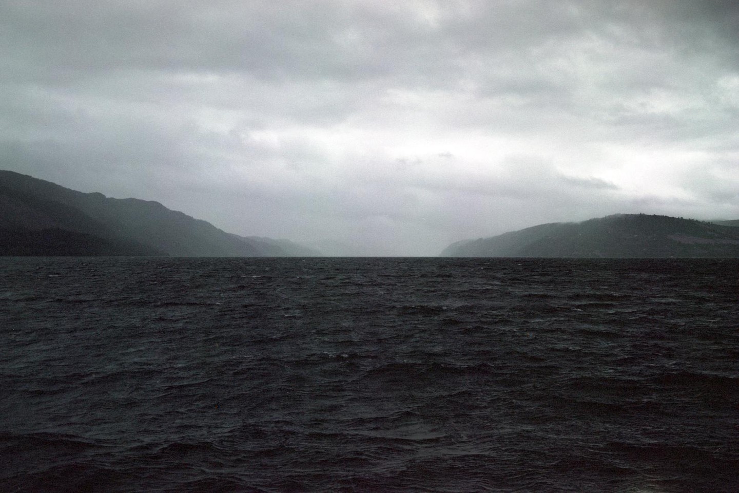 A wide body of water with mountains on either side is visible under a cloudy sky.