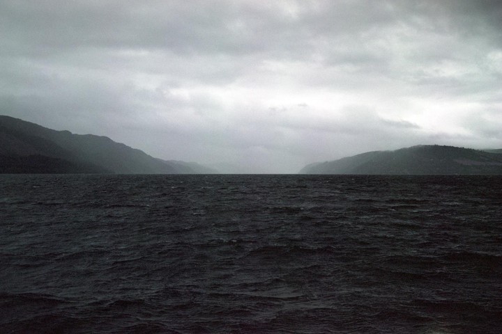 A wide body of water with mountains on either side is visible under a cloudy sky.