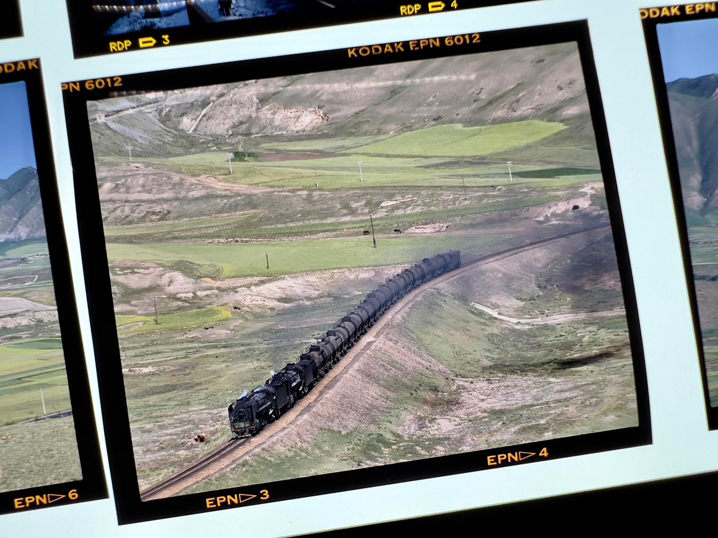 A long train with many cars travels through a green, hilly landscape.