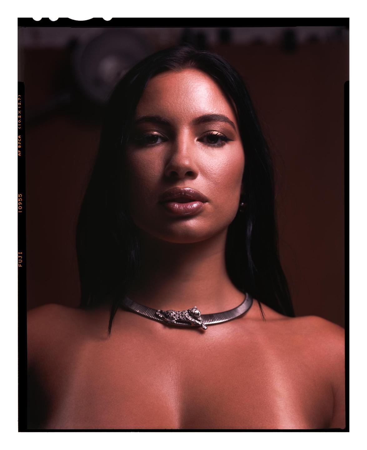 A woman with long dark hair and a metallic choker with a jaguar ornament looks directly at the viewer.