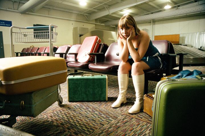 A woman sits on an airport bench surrounded by luggage.