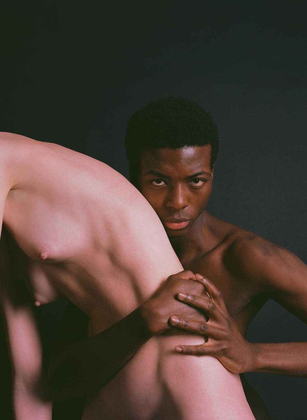 A man with dark skin holds a person with light skin, who is turned away from the camera.
