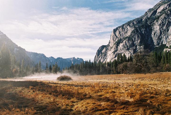 A foggy valley with mountains and pine trees is visible under a cloudy sky.