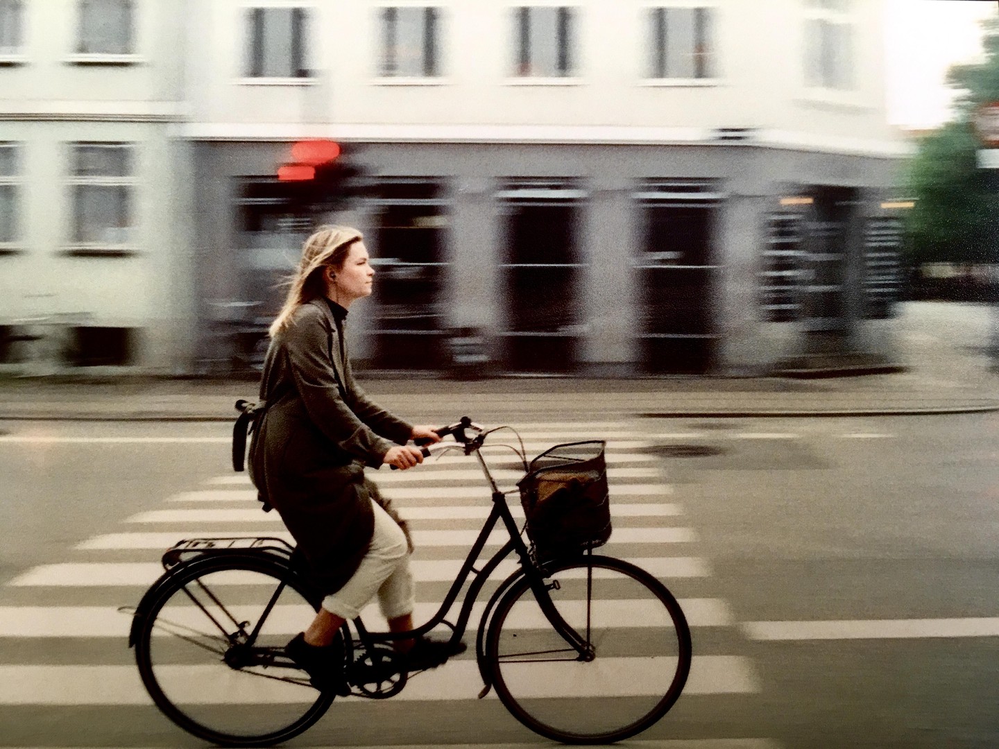 A woman rides a bicycle across a crosswalk in front of a building with blurred windows.