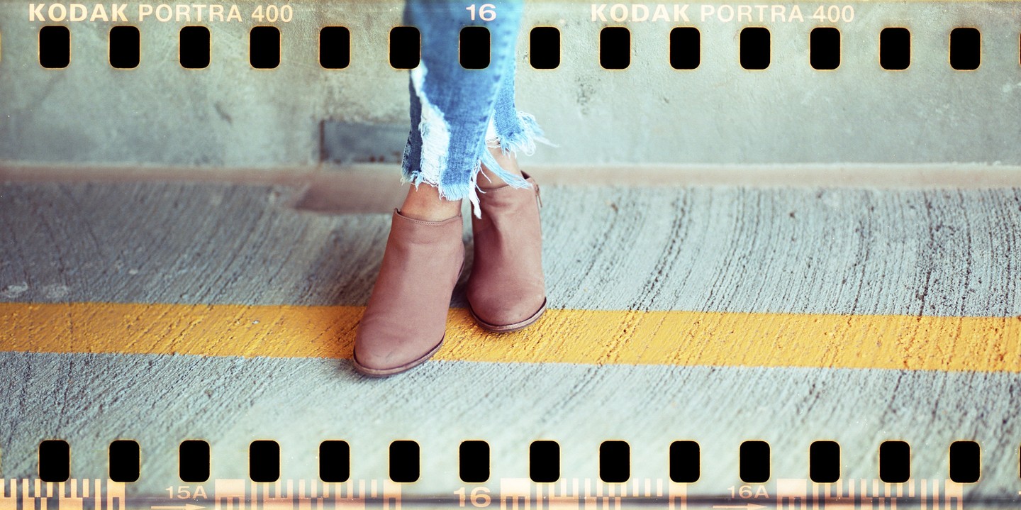A person wearing ripped jeans and brown boots stands on a concrete surface with a yellow line.