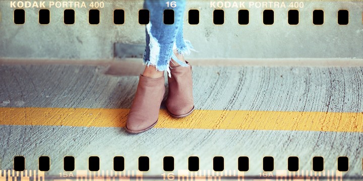 A person wearing ripped jeans and brown boots stands on a concrete surface with a yellow line.