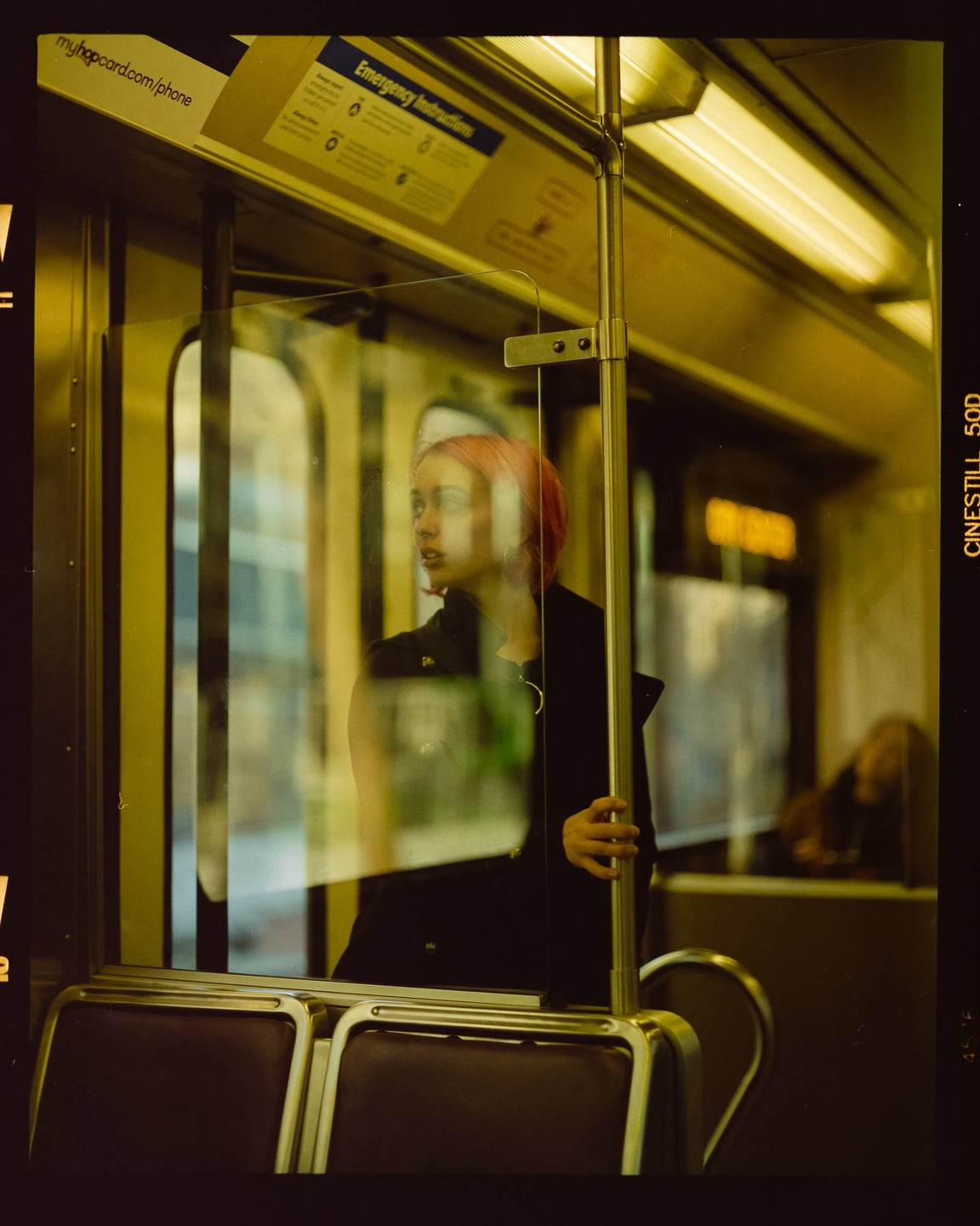 A woman with pink hair looks out a window on a train.