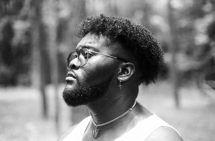 A man with a beard, glasses, and a cross earring looks up and to the right.