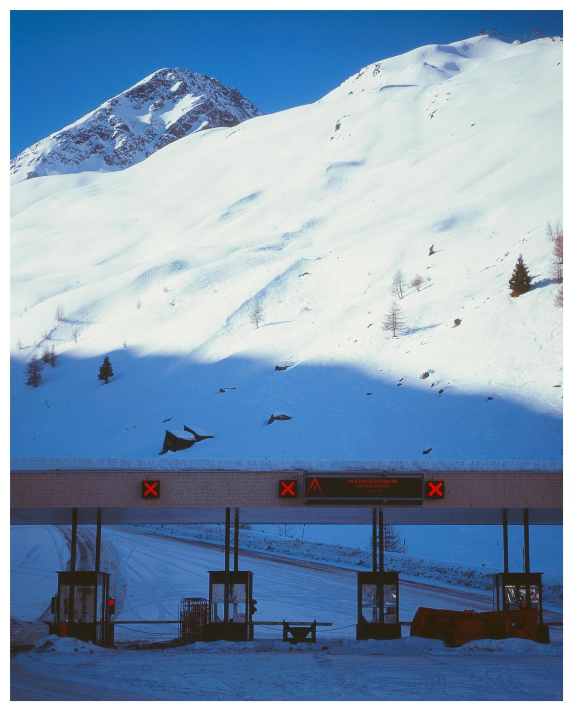 A toll booth is visible at the base of a snow-covered mountain.