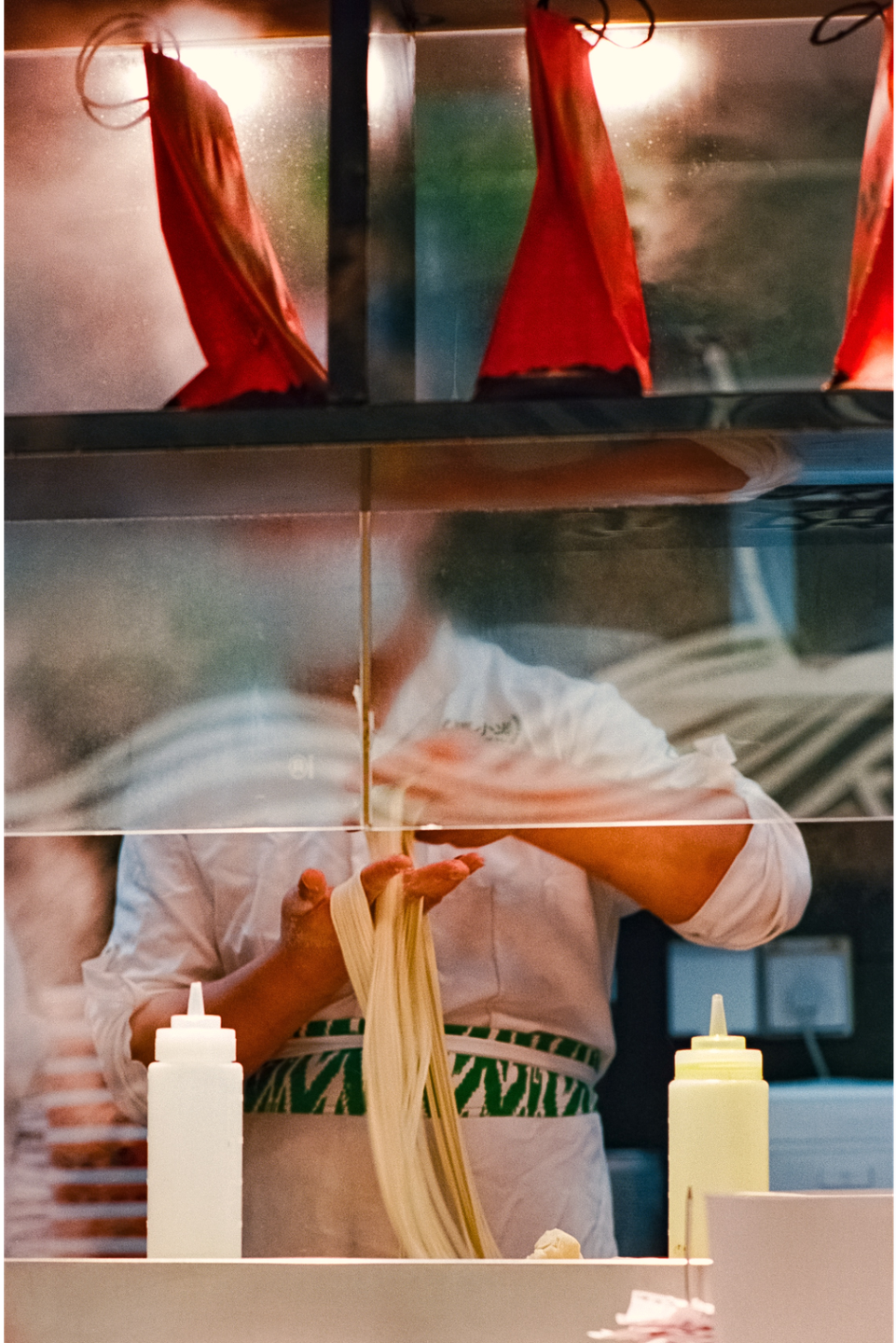 A chef is making hand-pulled noodles behind a glass counter.