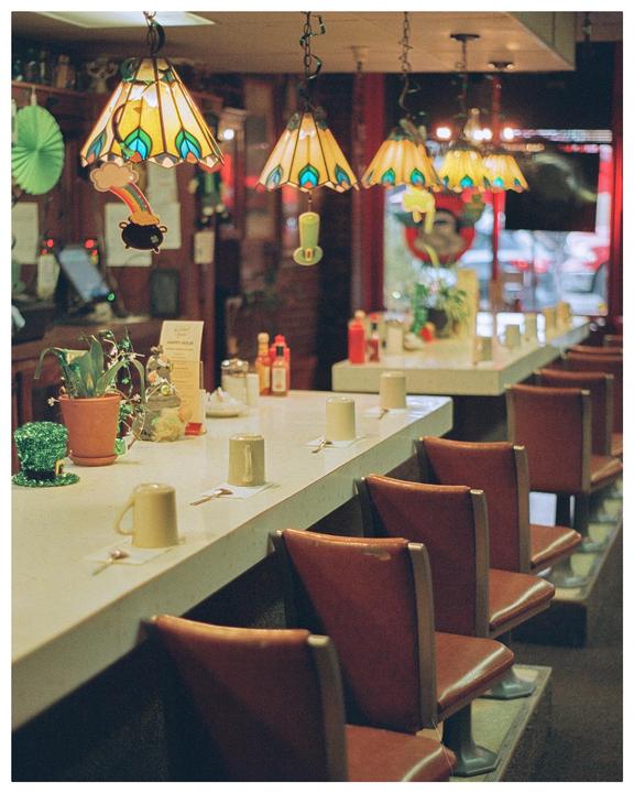 A diner counter with stools and stained glass lamps is decorated with St. Patrick's Day ornaments.
