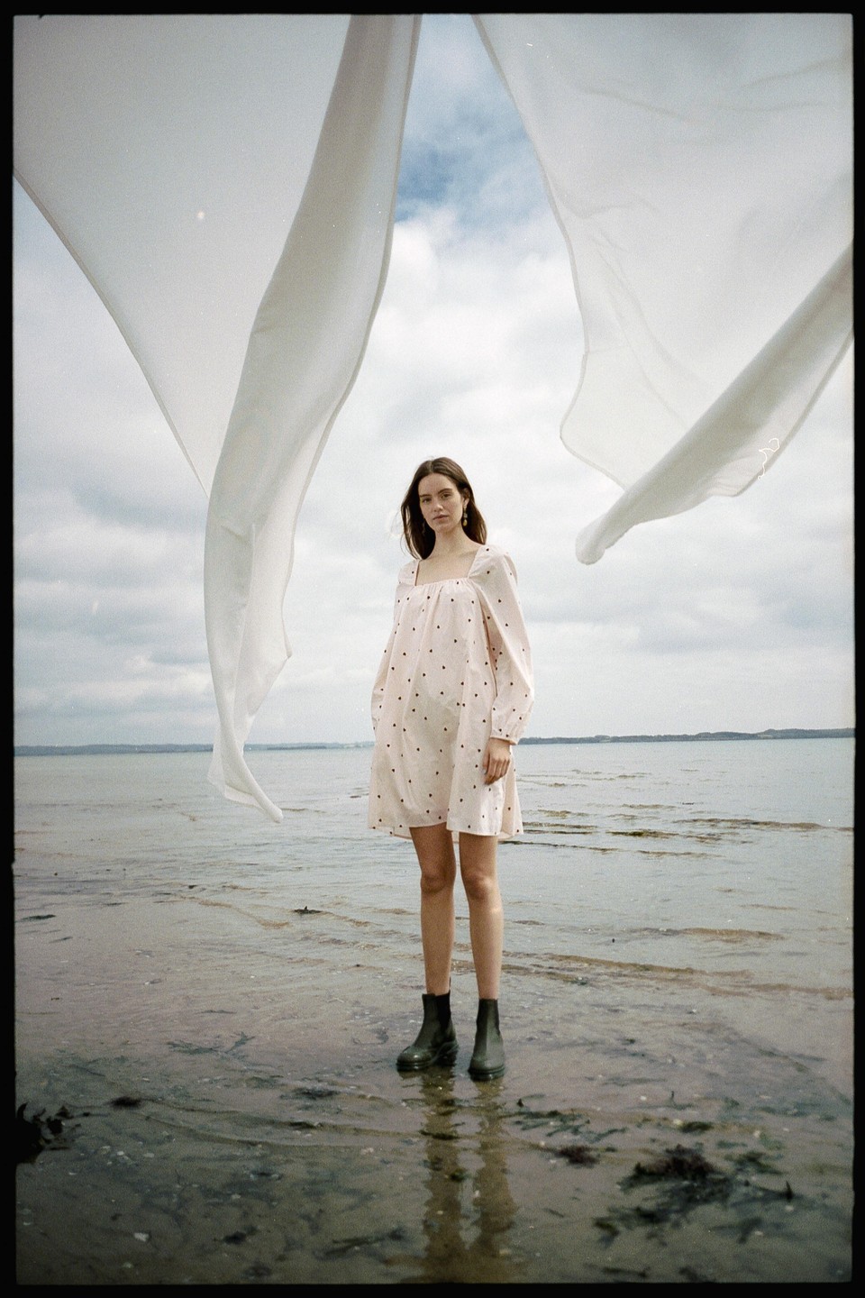 A woman stands in shallow water with two white cloths draped above her.