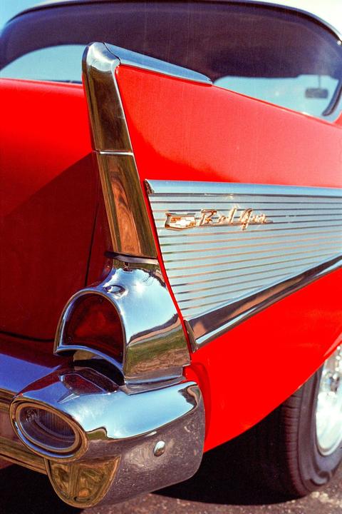 The rear quarter panel of a red Chevrolet Bel Air is visible, featuring a chrome tail fin and trim.