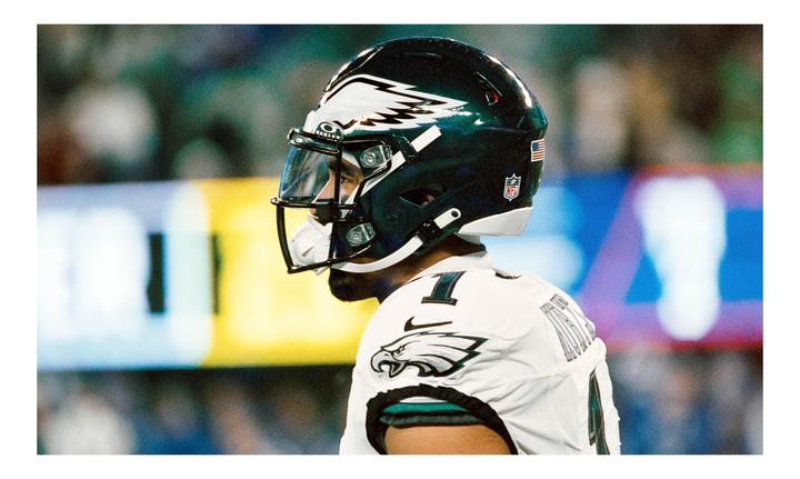 A football player in a white jersey and dark helmet with an eagle logo is shown from the side.