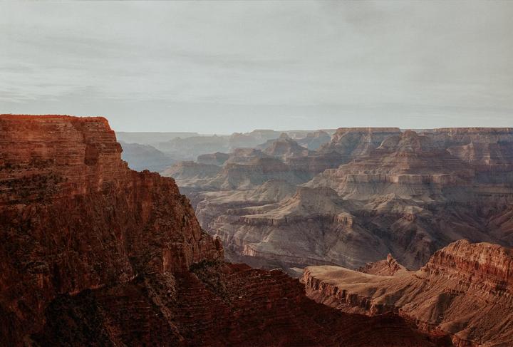 A vast canyon landscape with layered rock formations stretches under a hazy sky.