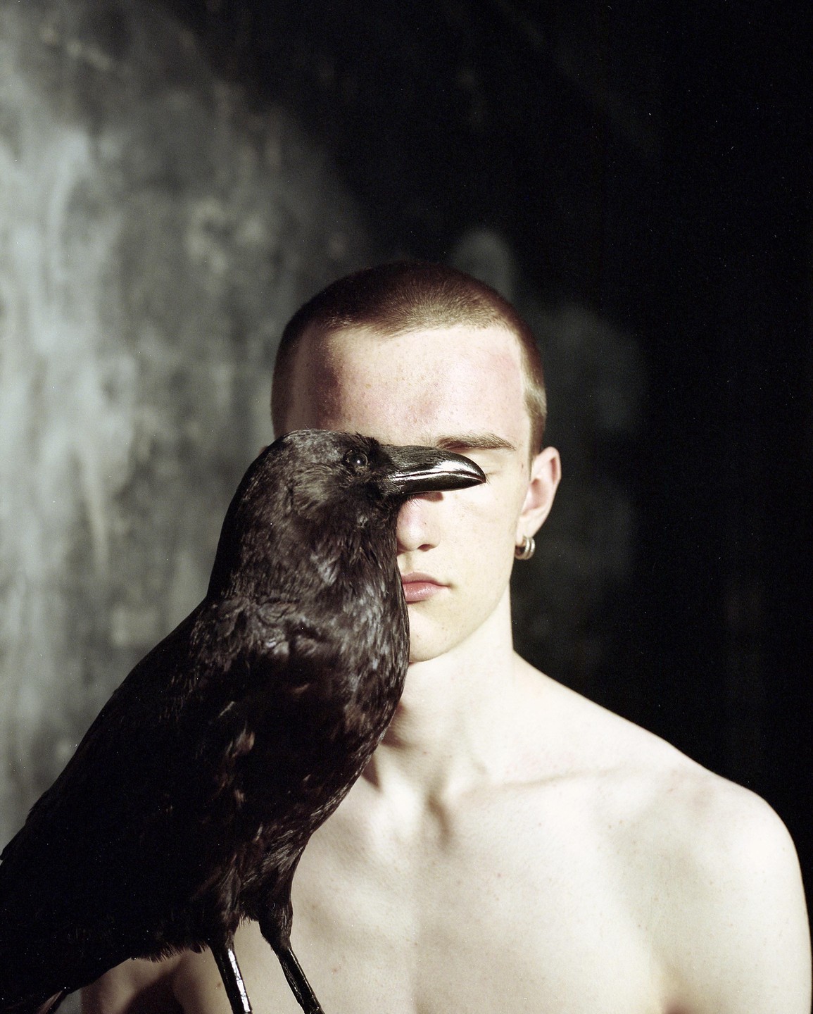 A crow stands in front of a man's face, obscuring one of his eyes.