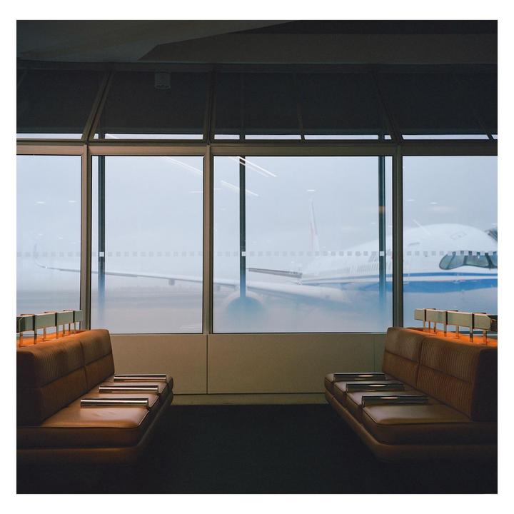Two brown benches face each other in an airport waiting area with a large window looking out onto an airplane.
