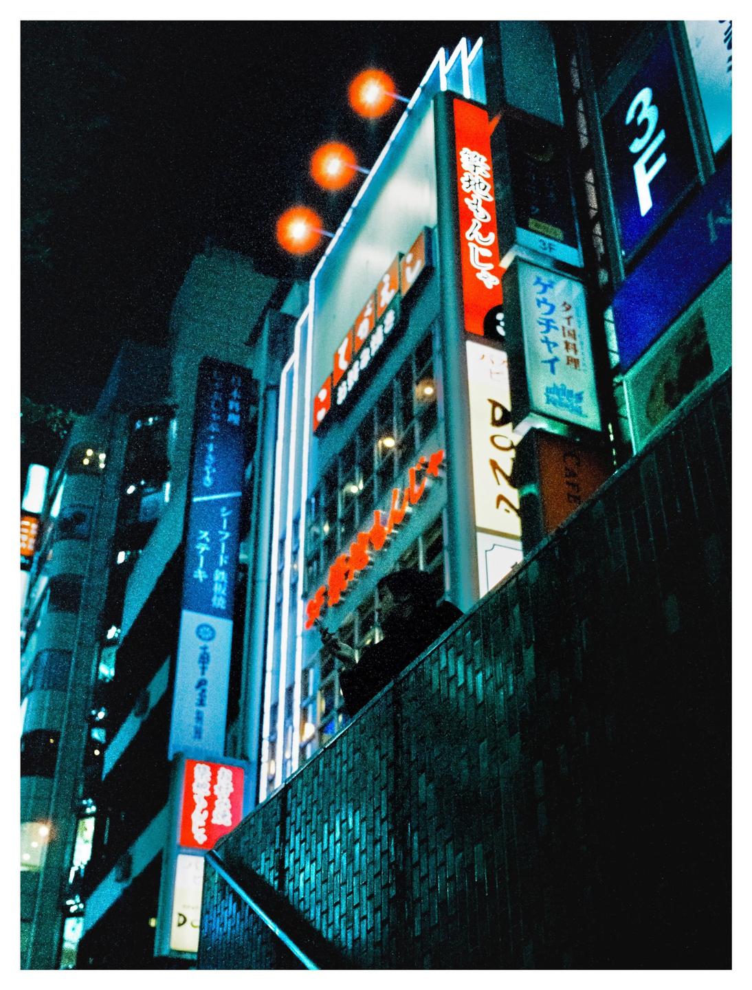 A tall building with many illuminated signs in Japanese and English stands out against the dark night sky.
