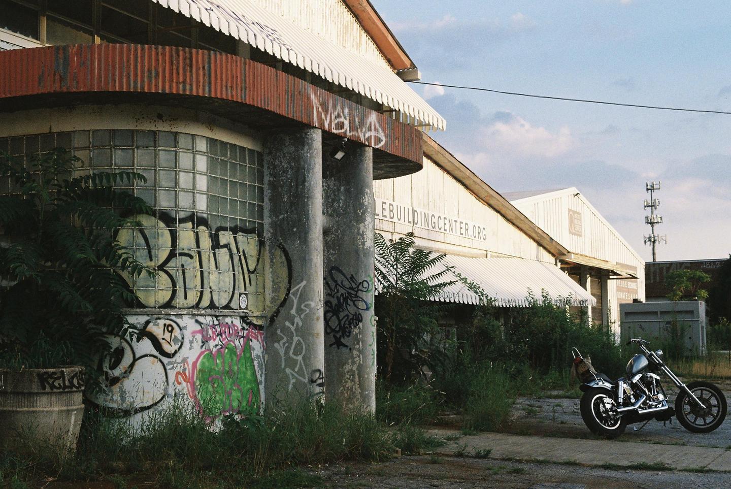 A motorcycle is parked on a paved area next to a building with awnings and graffiti.