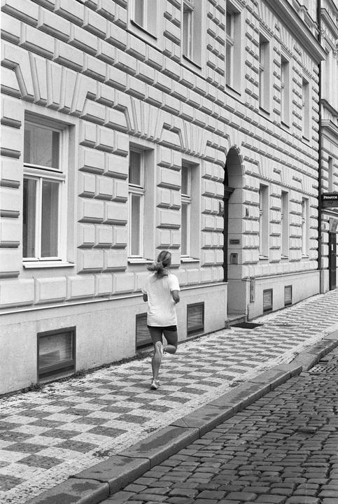 A woman runs along a checkered sidewalk next to a building with many windows.