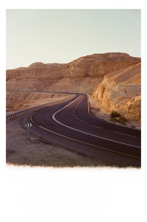 A winding road curves through a desert landscape with rocky mountains under a clear sky.