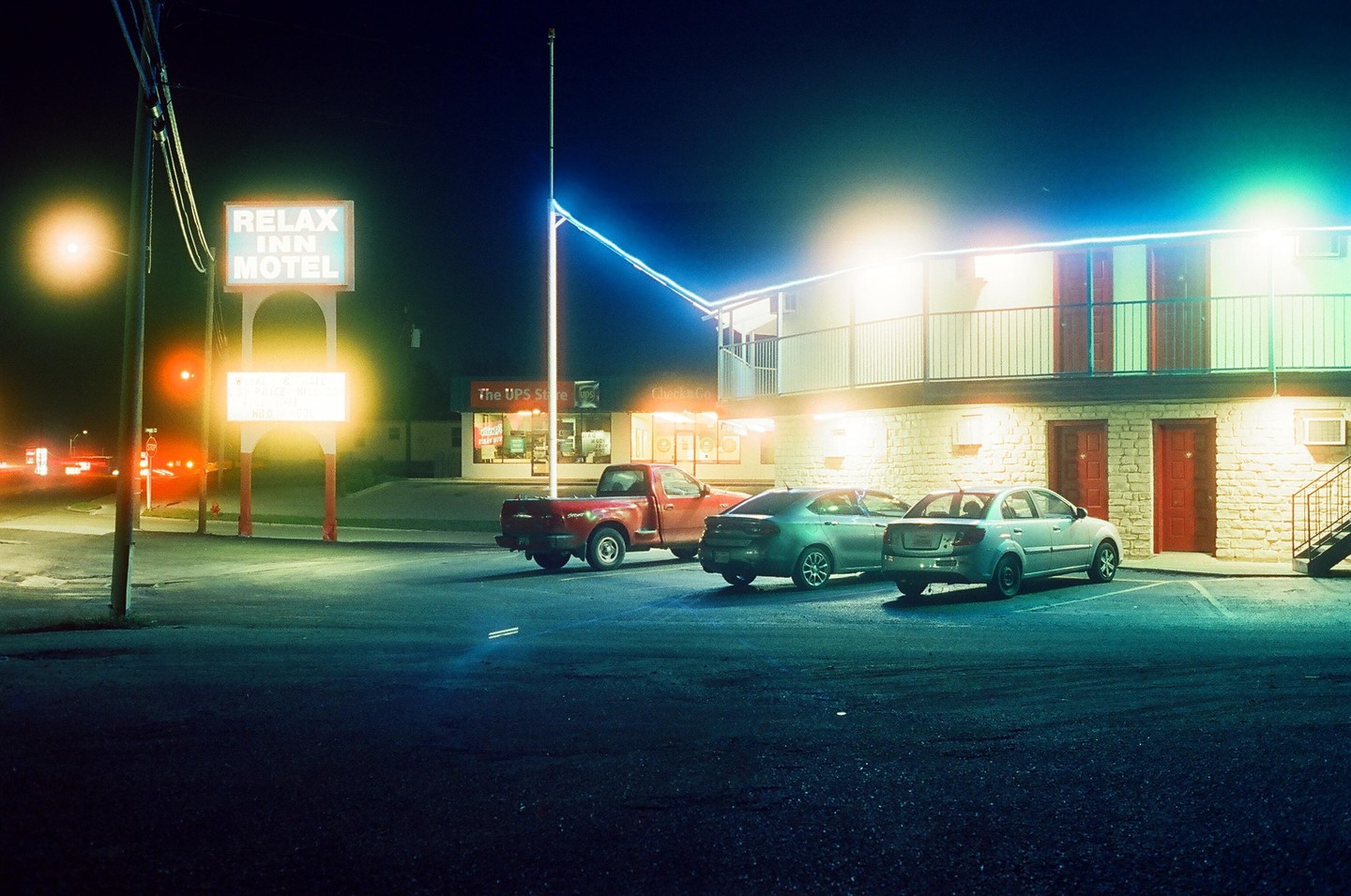 A motel sign and building are illuminated by neon lights at night, with several cars parked in front.