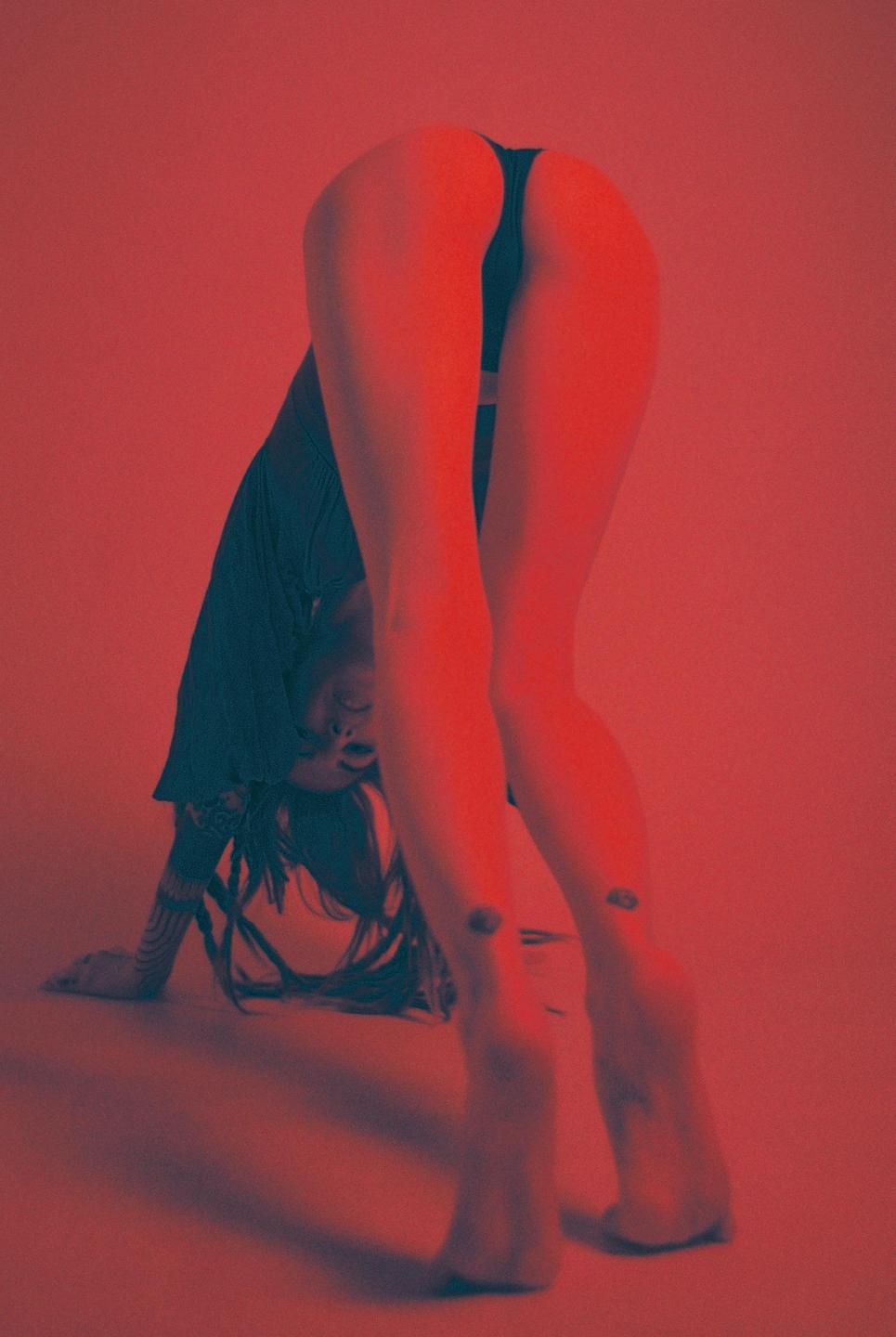 A woman bends over with her head near the floor, illuminated by red light.
