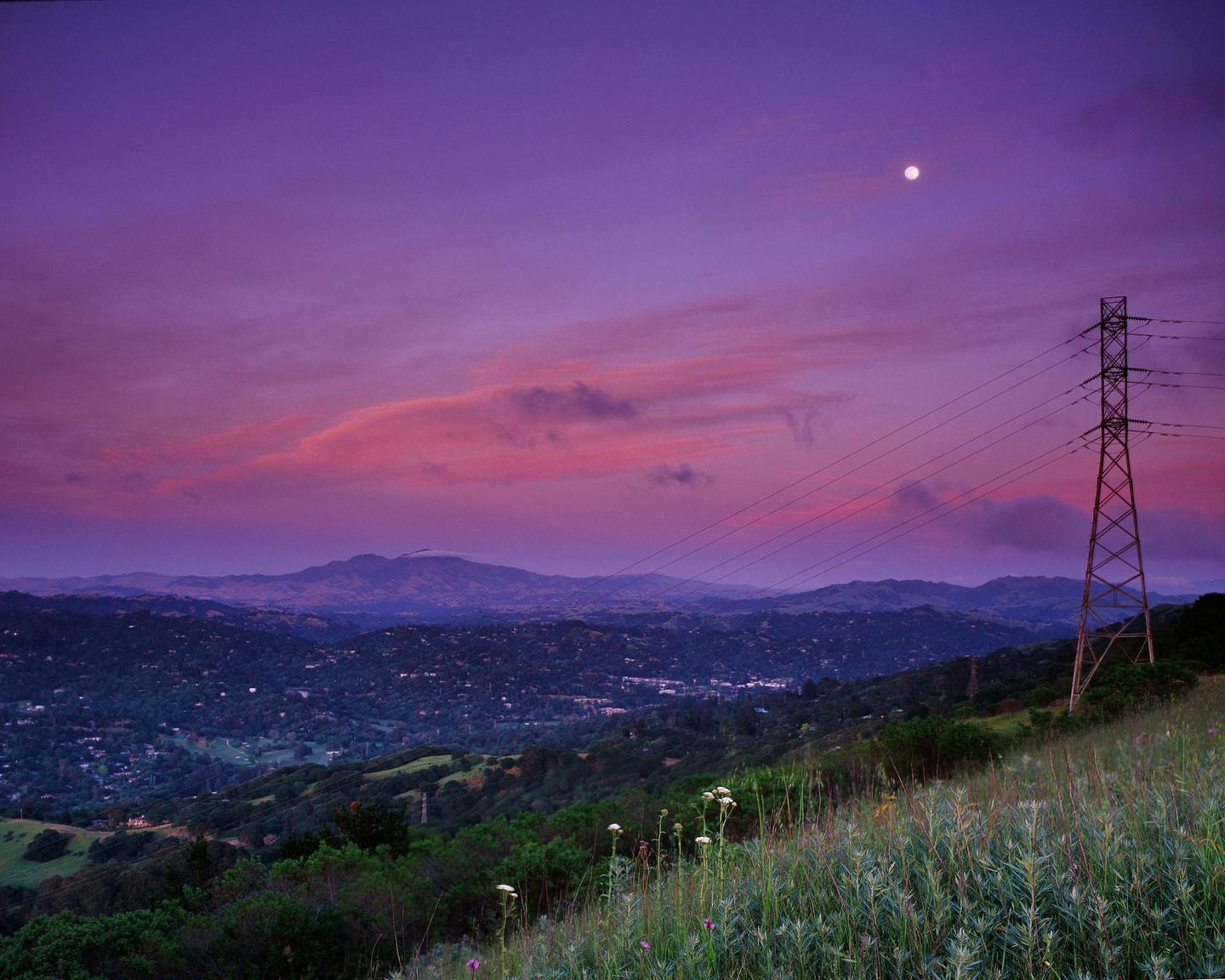 A full moon is visible in a purple and pink sky over a mountainous landscape with a power line tower in the foreground.