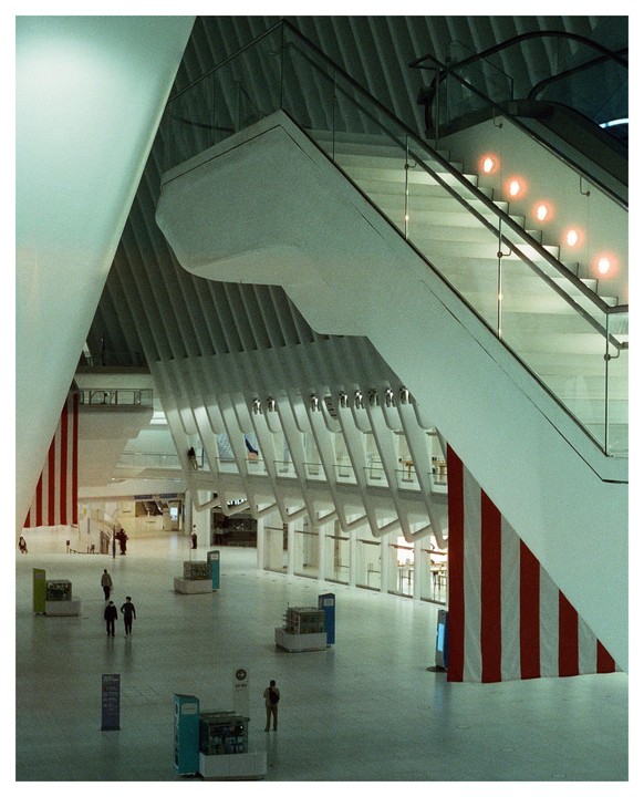 People walk around a large, modern interior space with escalators and red and white striped banners.