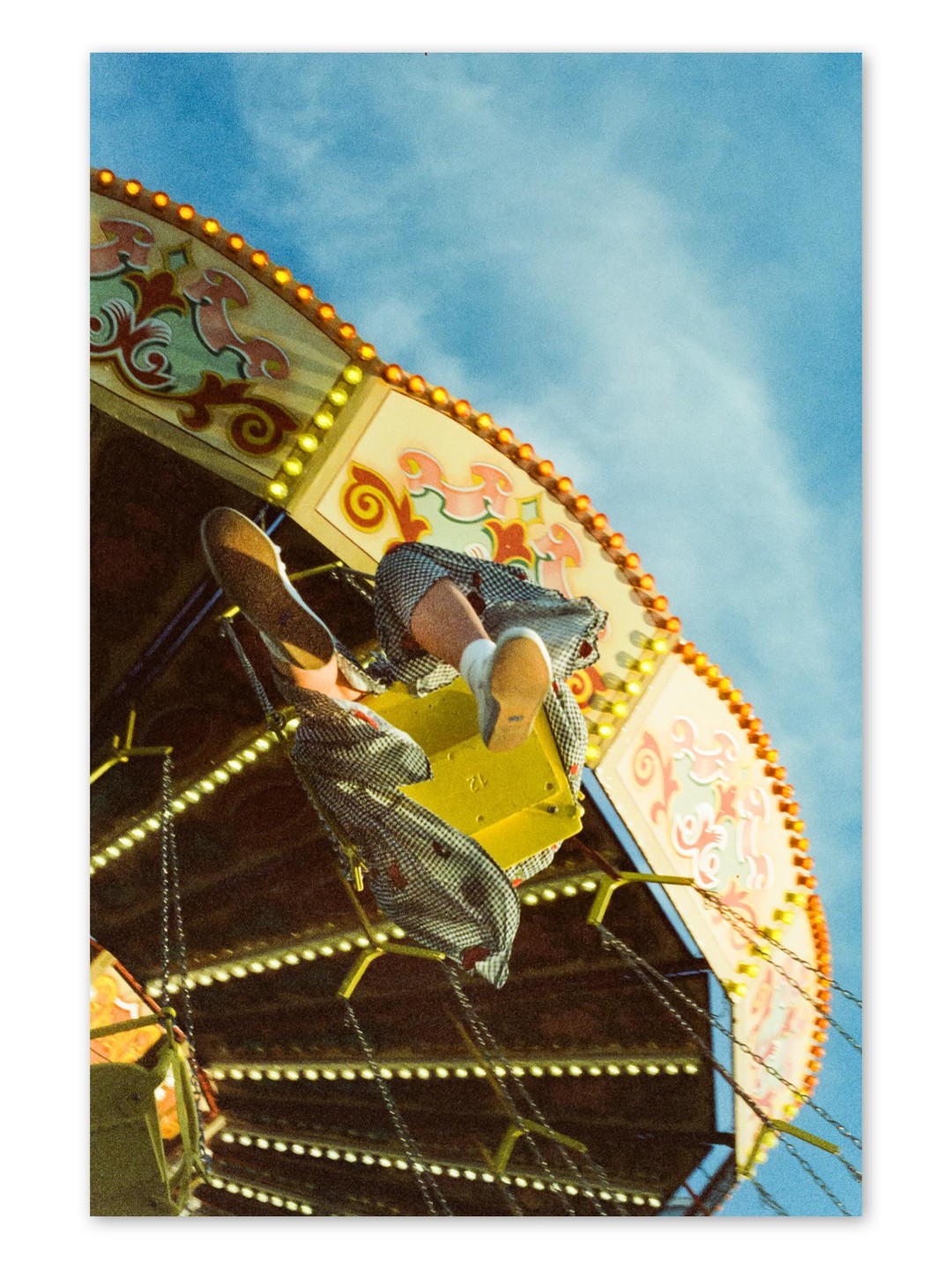 A person's legs and feet are visible as they ride a swing ride at a fairground.