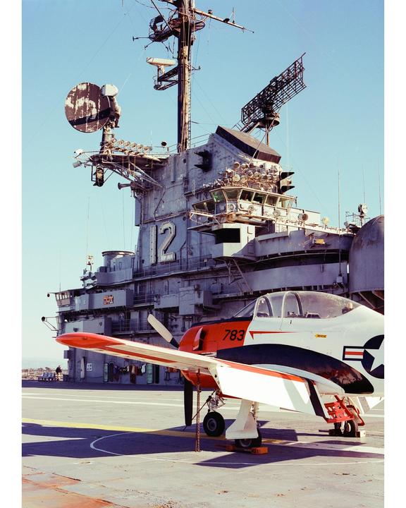 A small propeller plane is parked on the deck of a large aircraft carrier.
