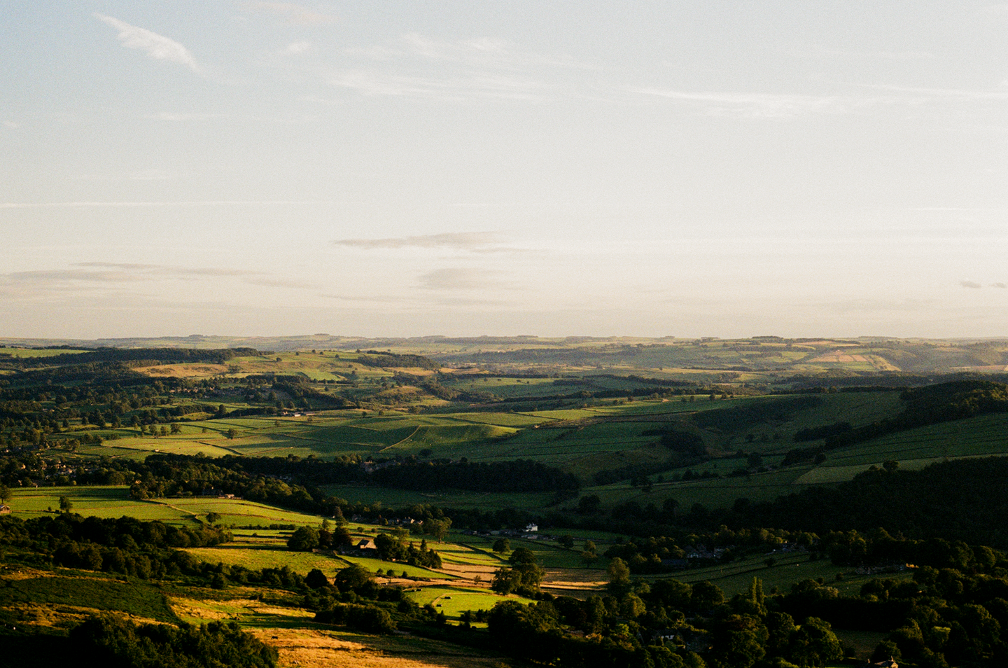 A vast landscape of rolling green hills and valleys stretches under a bright sky.