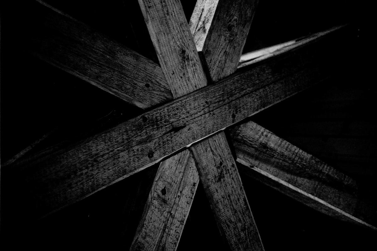 Several wooden beams are arranged in a crisscross pattern against a dark background.