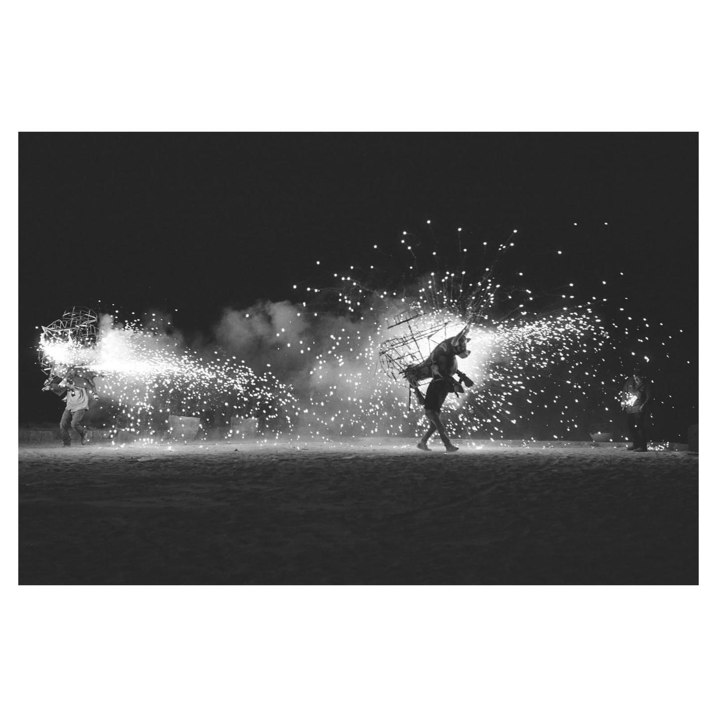 Two men in costume walk across a dark field at night, surrounded by fireworks.