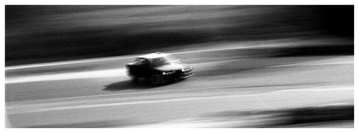 A car is captured in motion blur on a road.