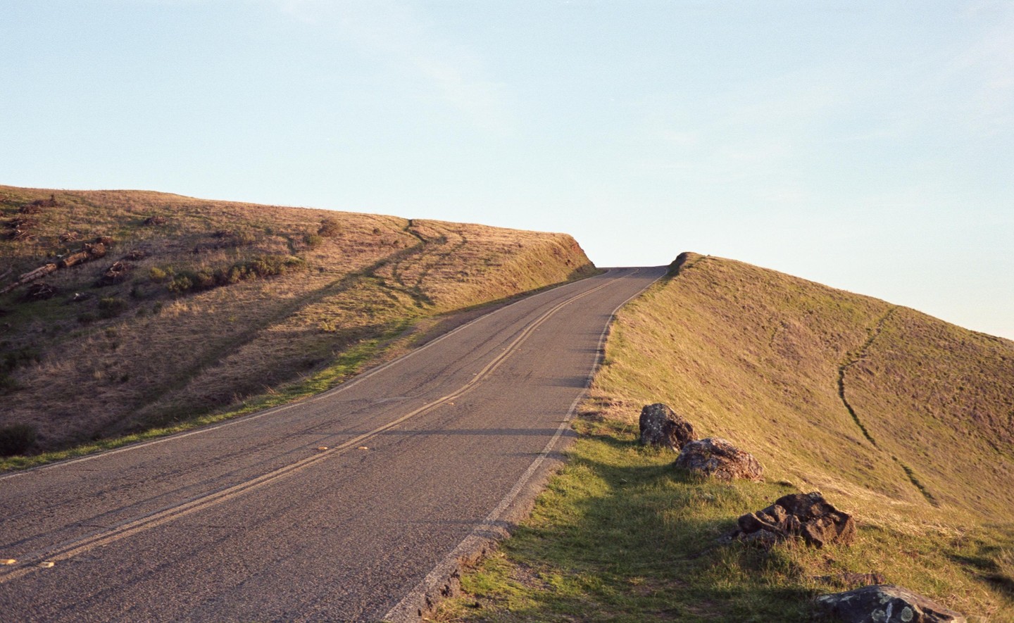 A paved road curves up a grassy hill under a clear sky.