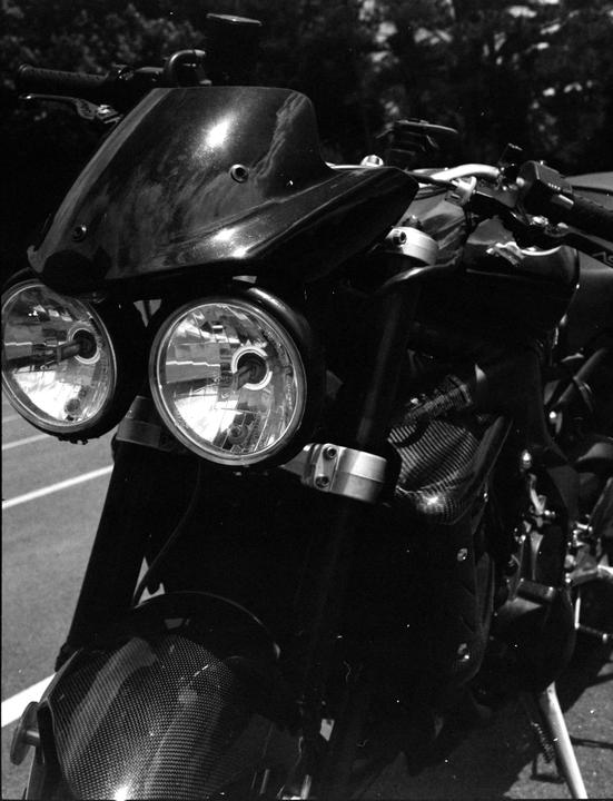 A black and white close-up shows the front of a motorcycle with two headlights and a small windshield.