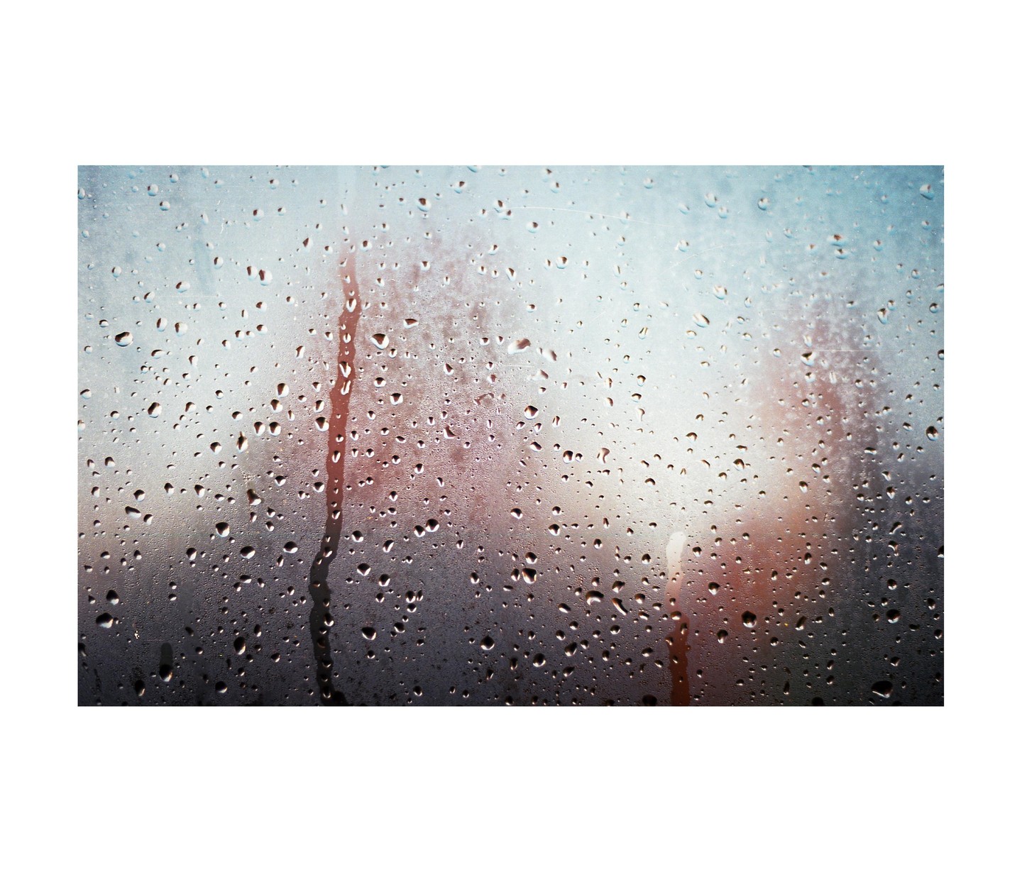 Raindrops cling to a window, blurring the warm-toned scene outside.