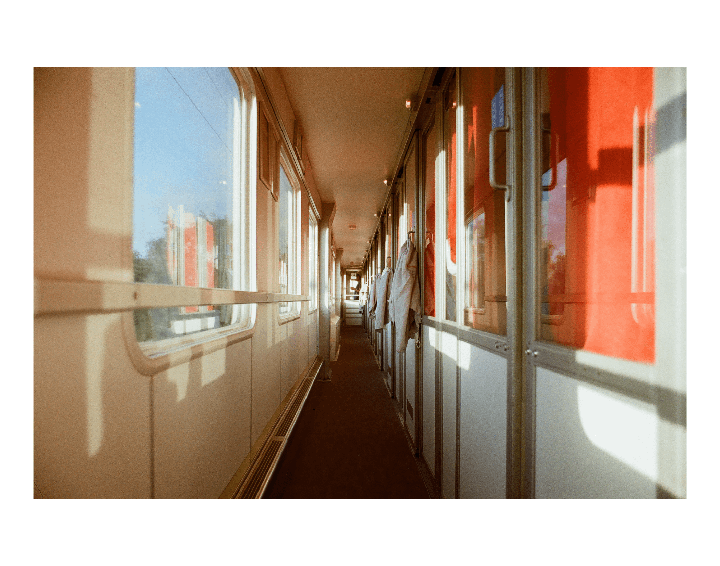 A long, narrow train corridor is visible with windows on the left and compartment doors on the right, some of which reflect a bright red color.