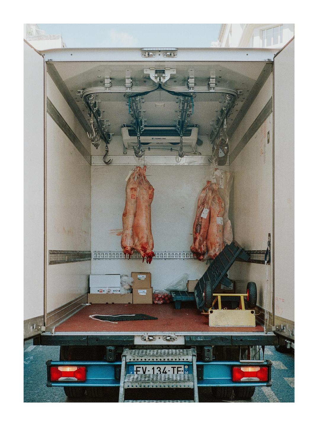 Two animal carcasses hang inside the back of a refrigerated truck.