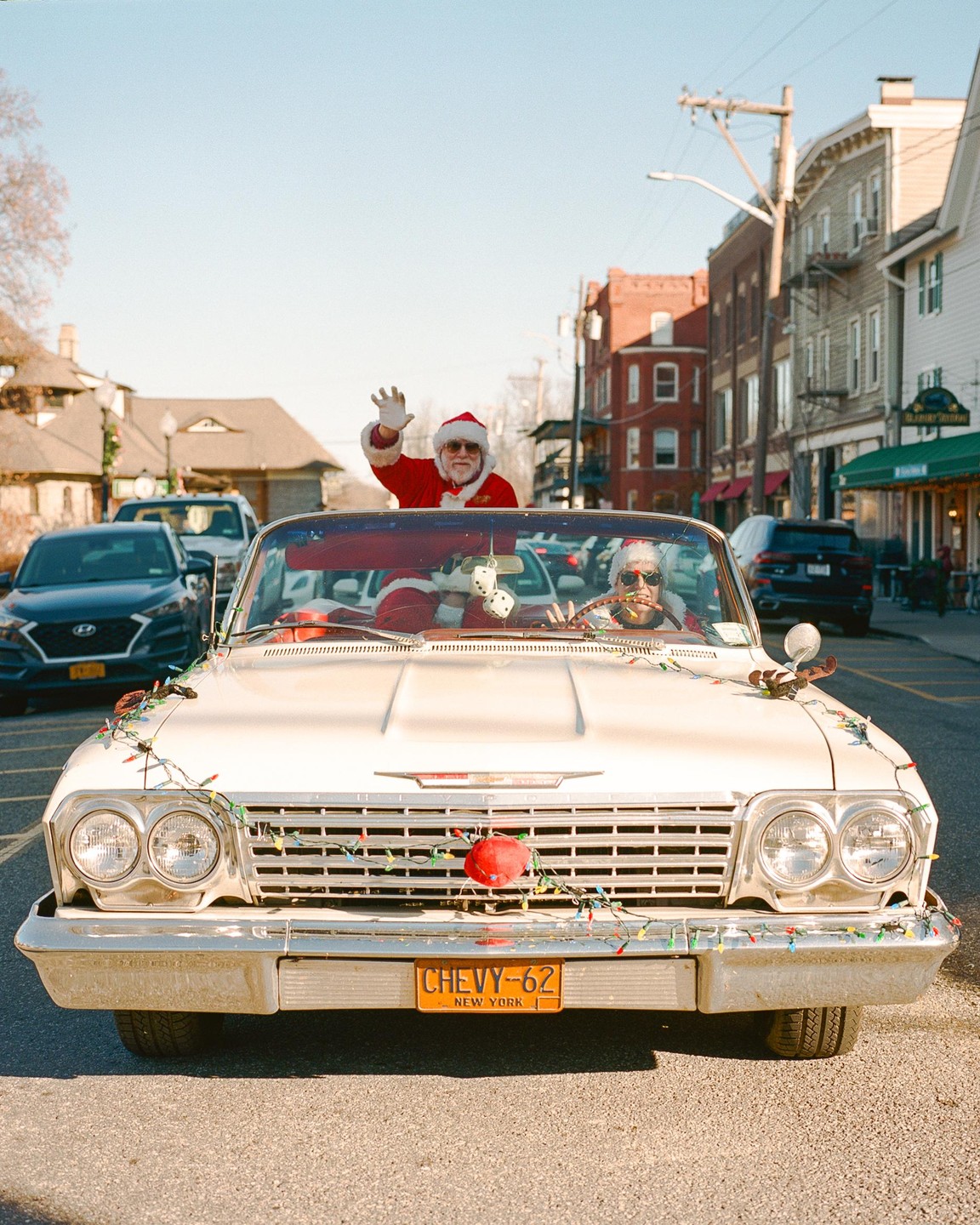 Two men dressed as Santa Claus drive a vintage convertible decorated with Christmas lights down a street in New York.